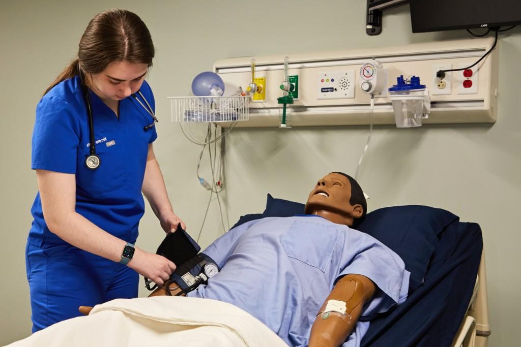 A physician assistant student practices taking blood pressure on a patient simulator